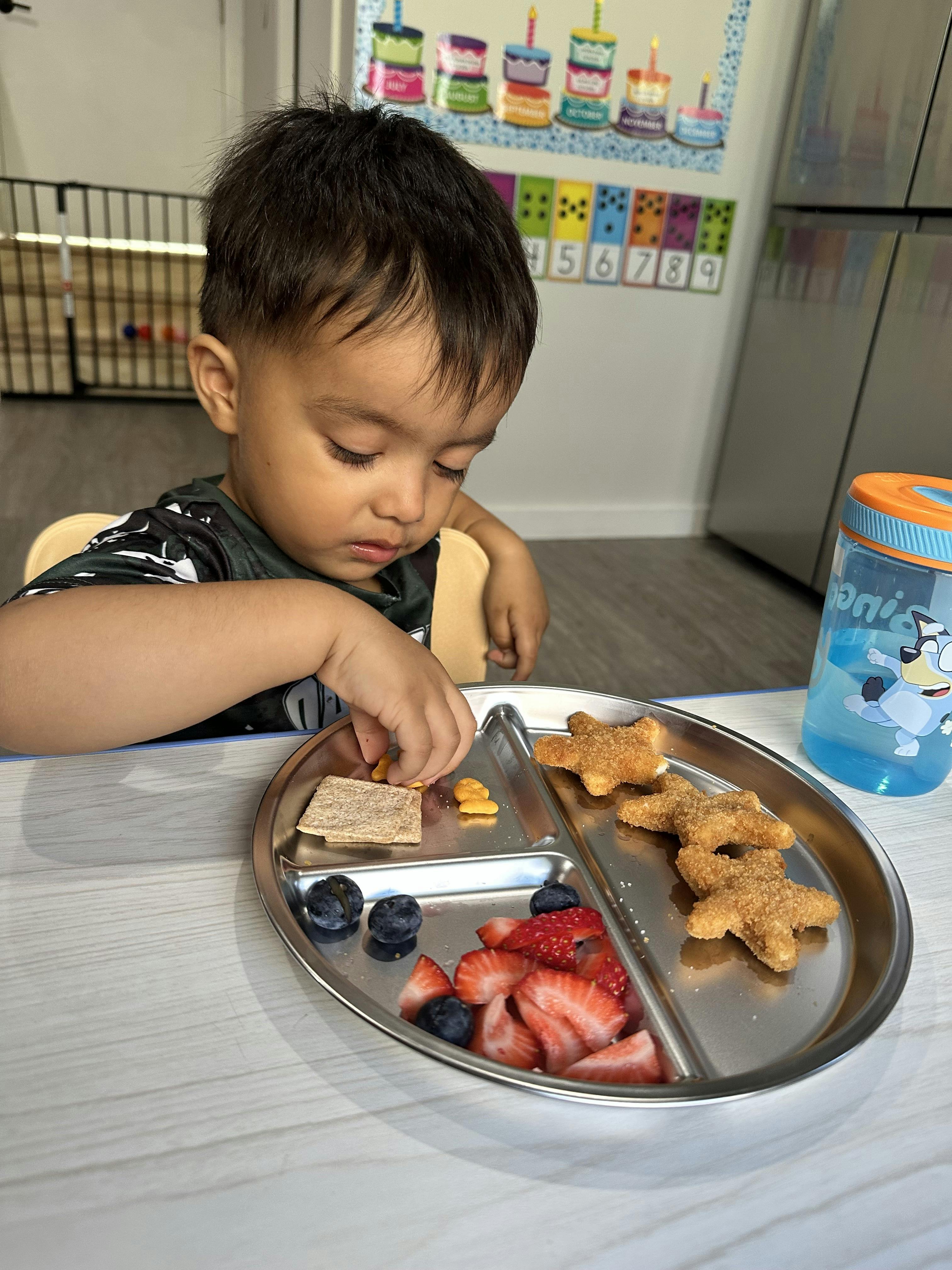 Child sitting at a table eating from a metal tray of food