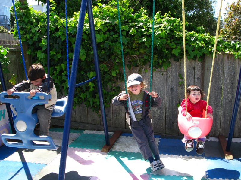Three children playing on swings in a yard