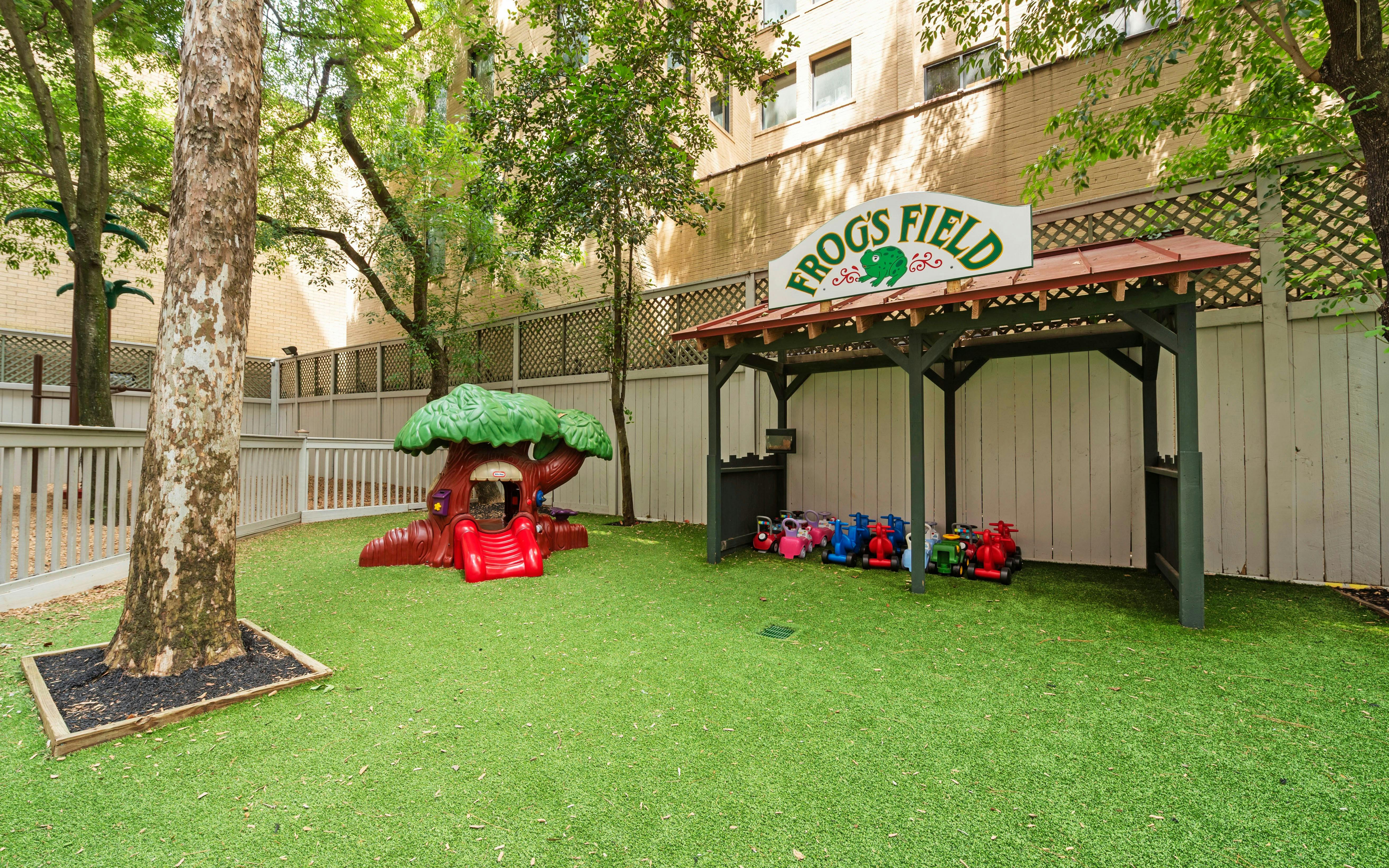 Playground area with artificial turf, a tree-shaped play structure, and ride-on toys