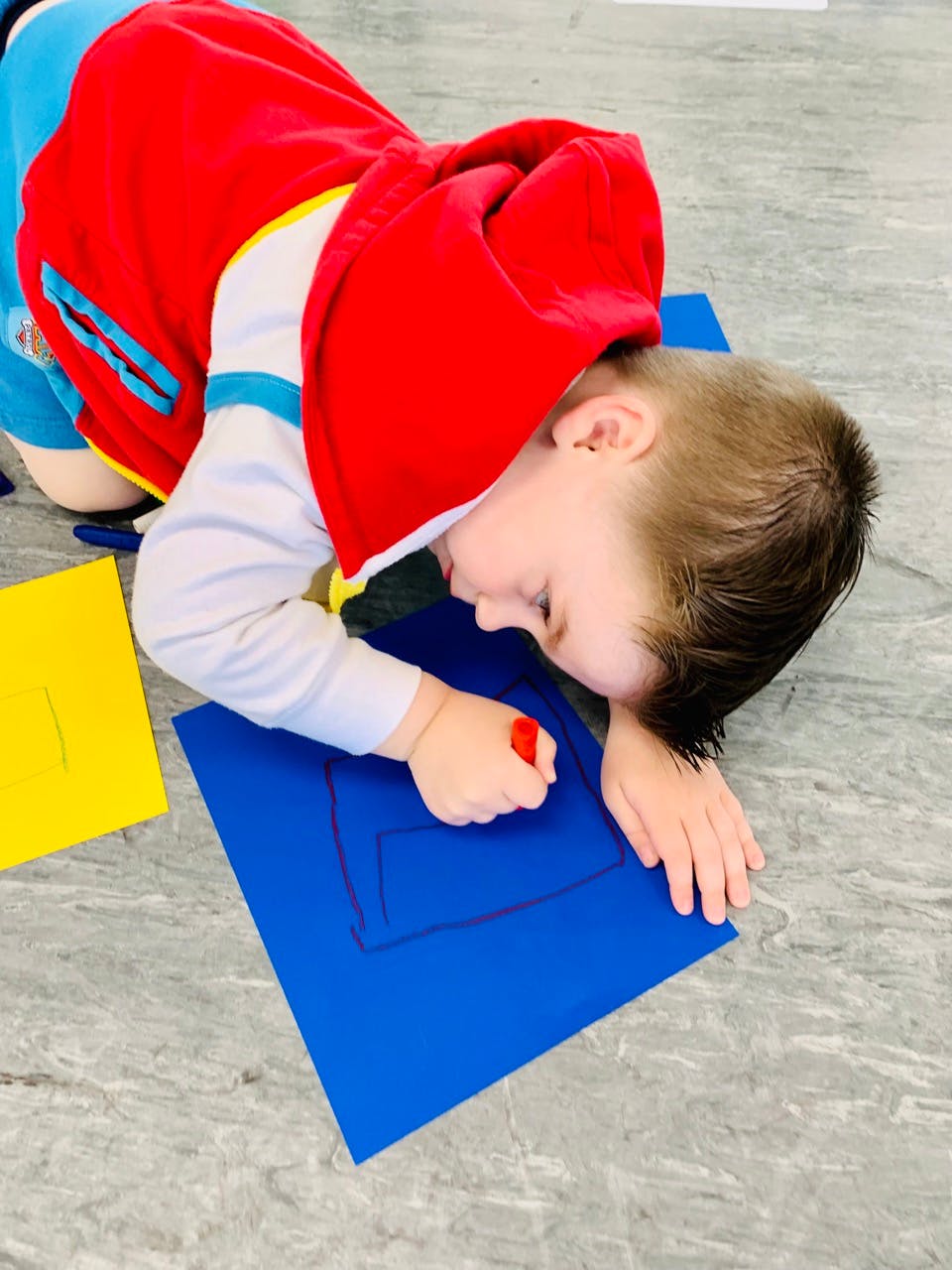 Child drawing on blue paper with a red marker