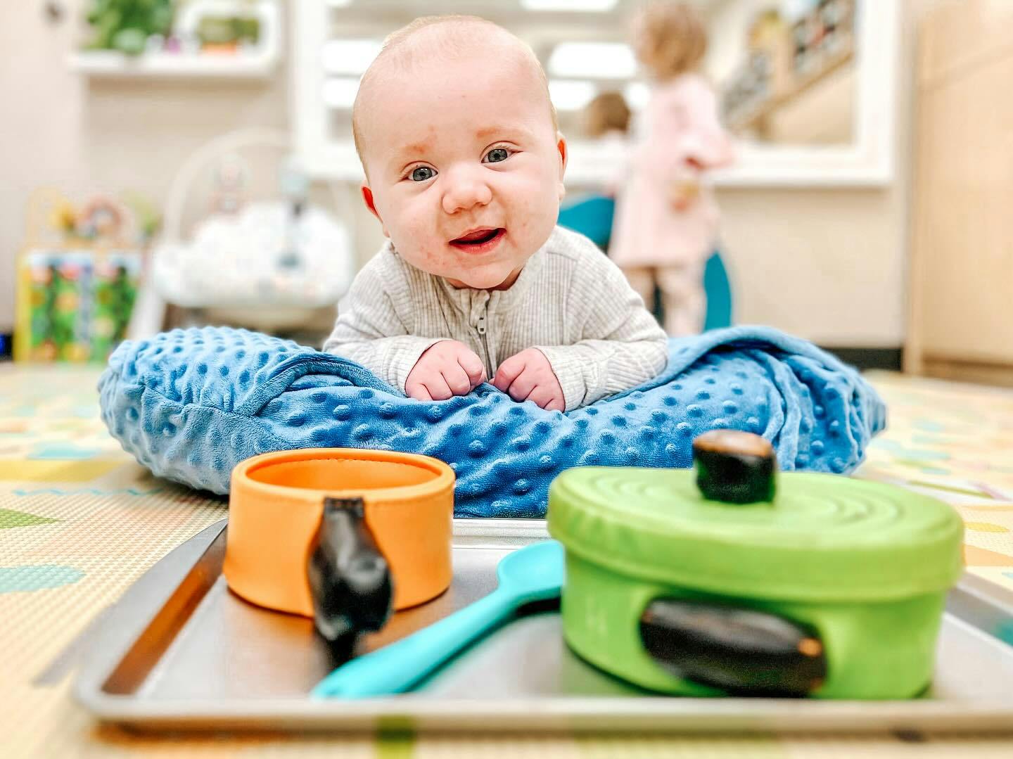 Child on a blue blanket with toy cooking pots