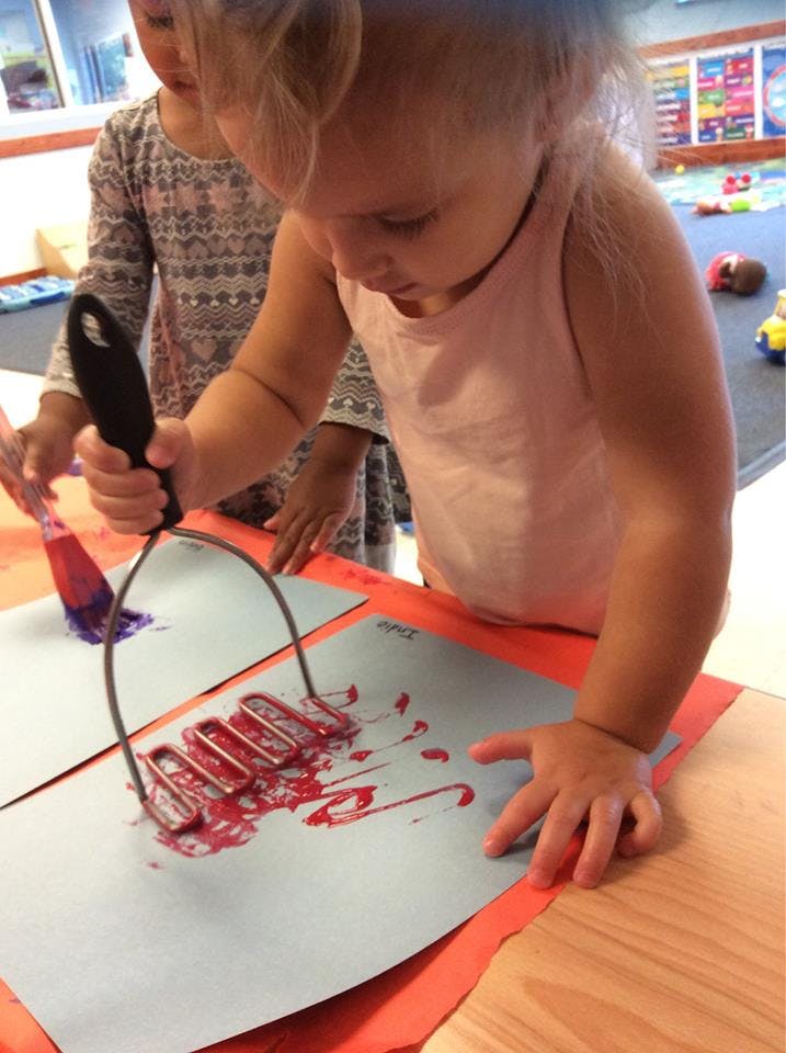 Child using a potato masher to spread red paint on paper