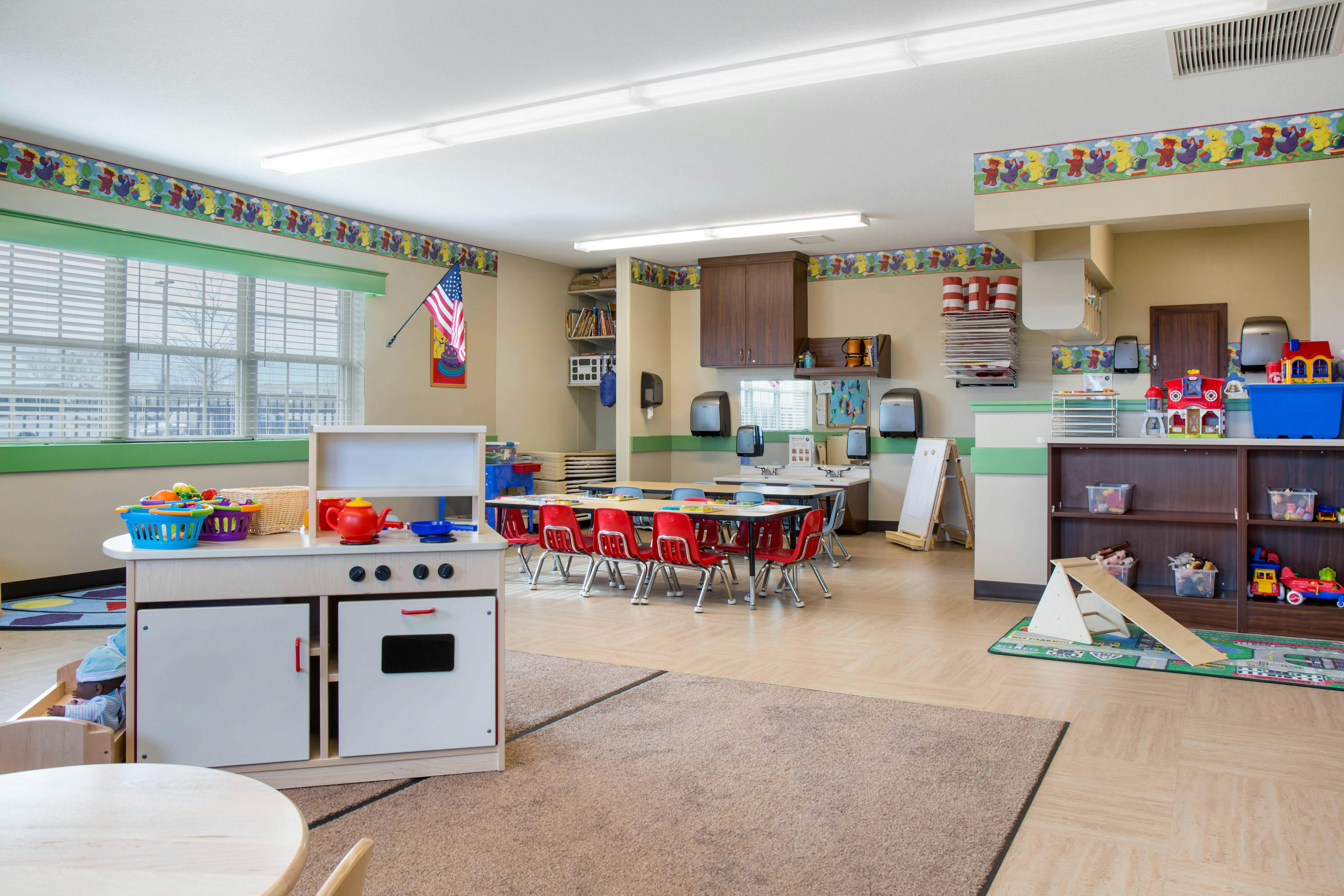 Classroom with play kitchen, small tables with red chairs, and shelves of toys