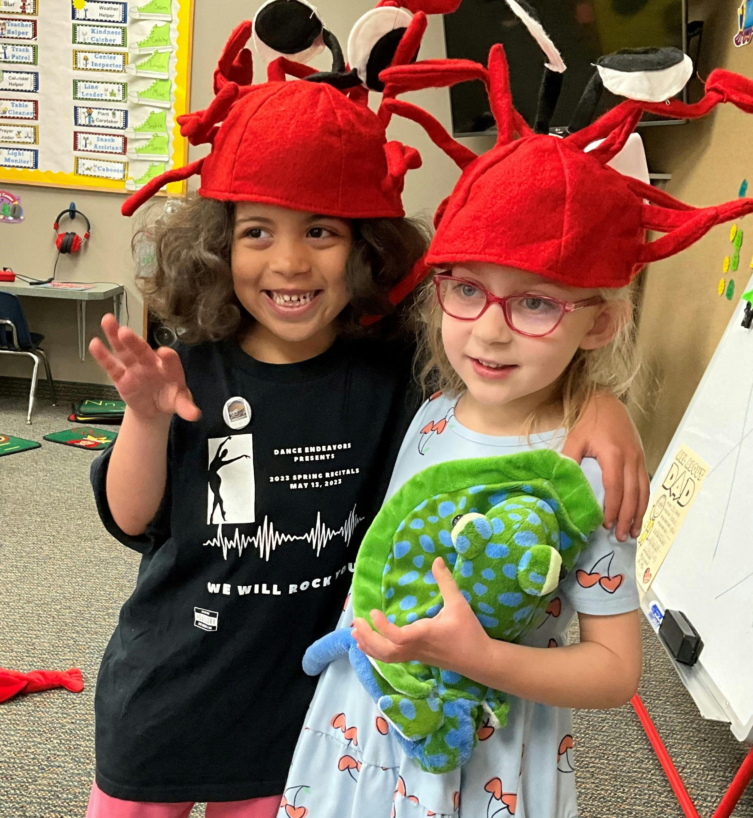 Two children wearing red crab hats, one holding a stuffed animal
