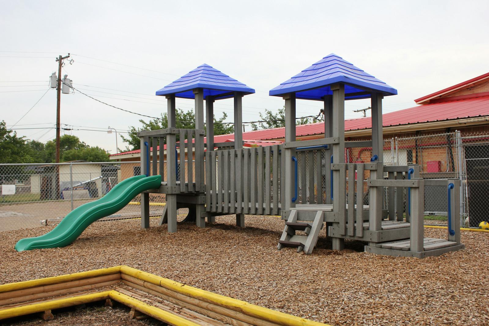 Playground structure with two towers, a green slide, and wood chip ground