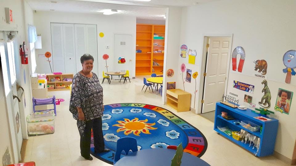 Person standing in a classroom with a sun rug