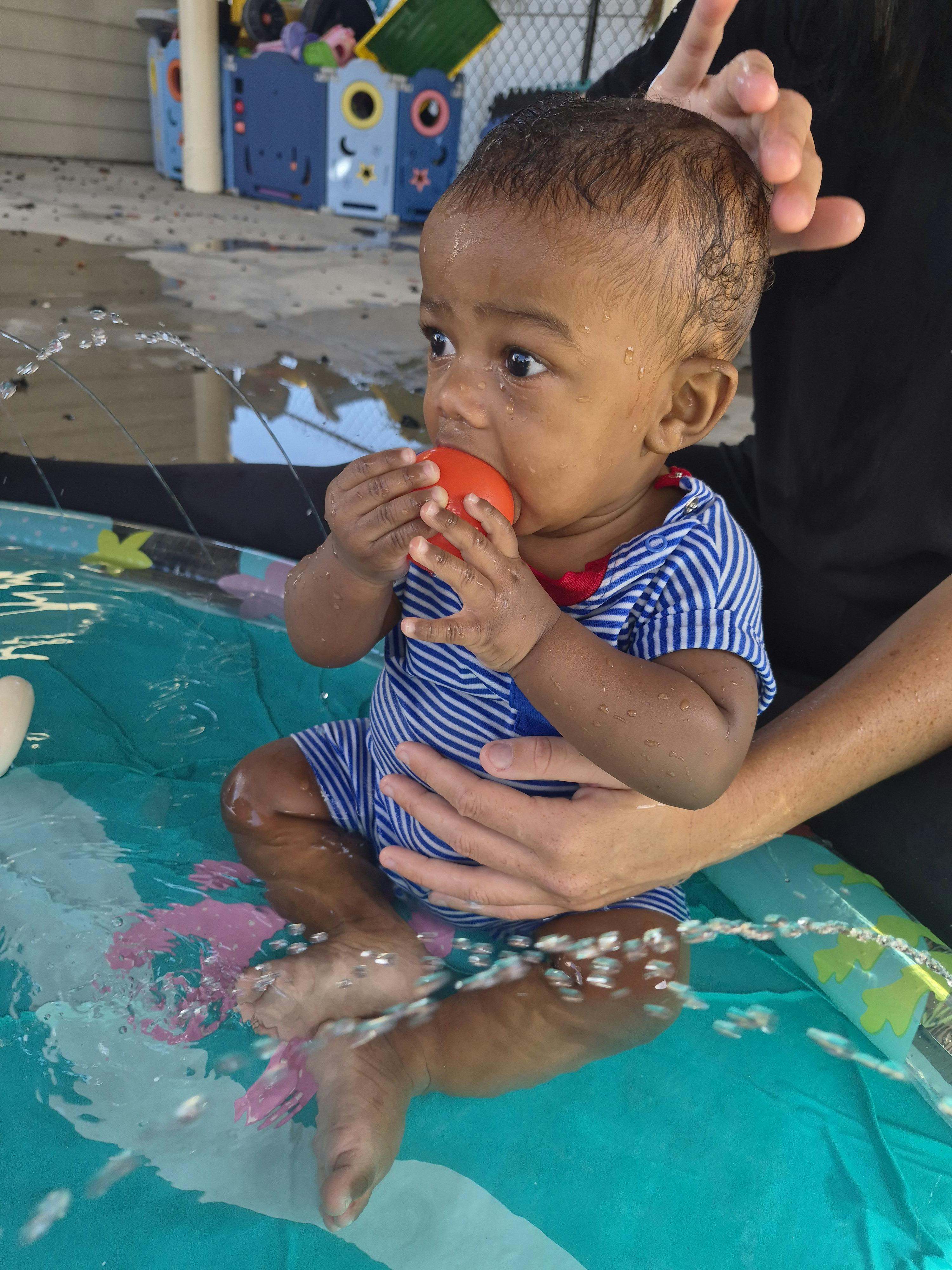 Child sitting in a small pool with a person holding them