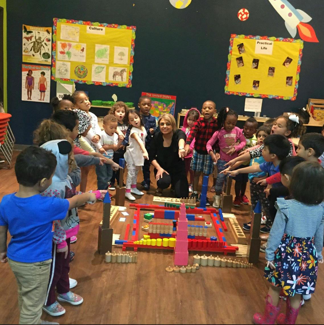 Adult and children gathered around a block structure in a classroom
