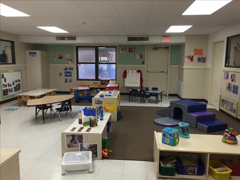 Classroom with tables, chairs, play equipment, and shelves with toys