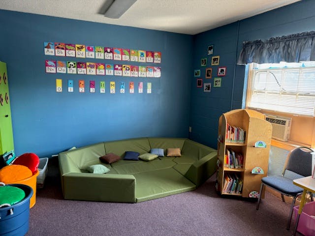Classroom with green sectional seating, bookshelf, and alphabet cards on wall