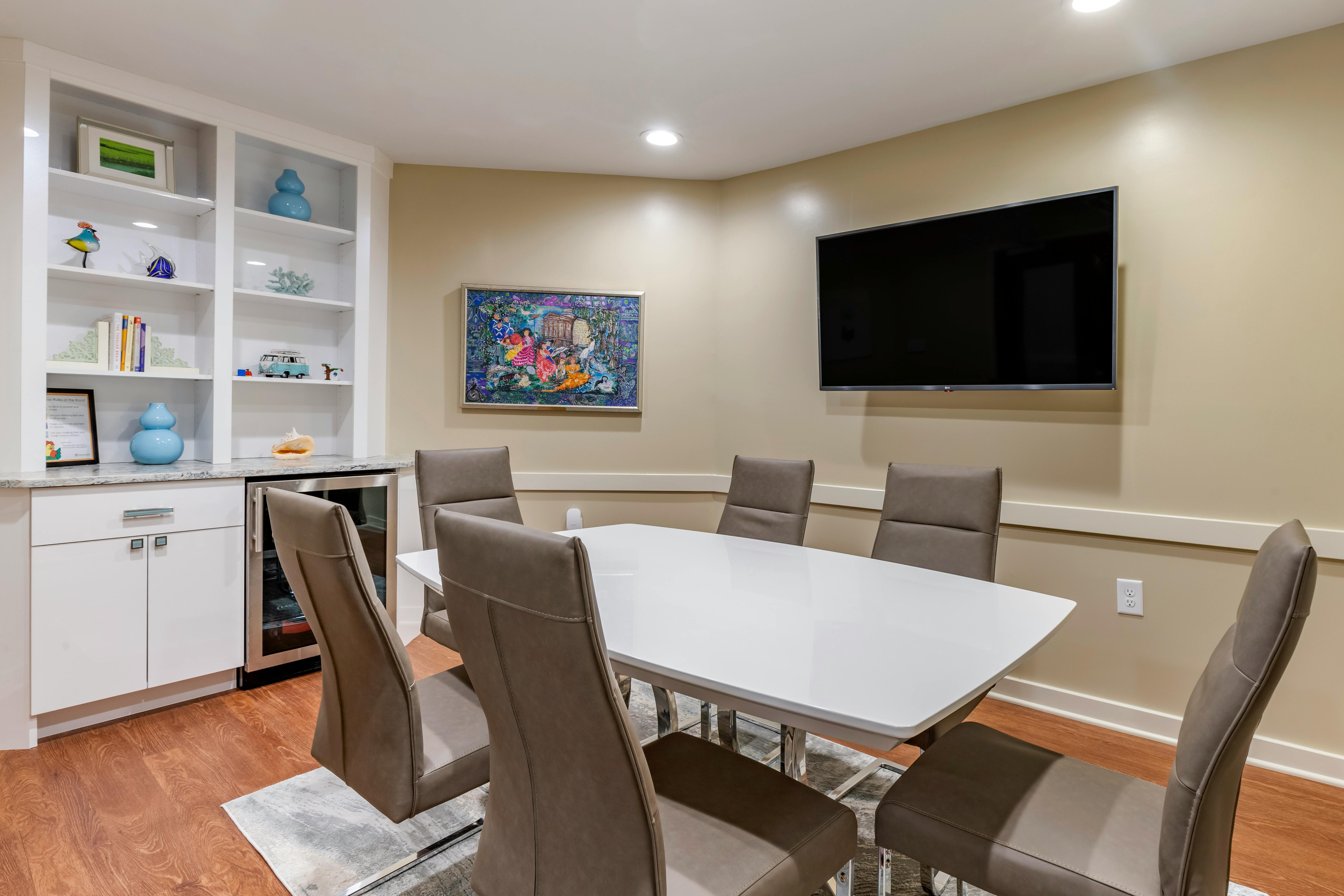 Meeting room with a white table and grey chairs, shelves, and a TV