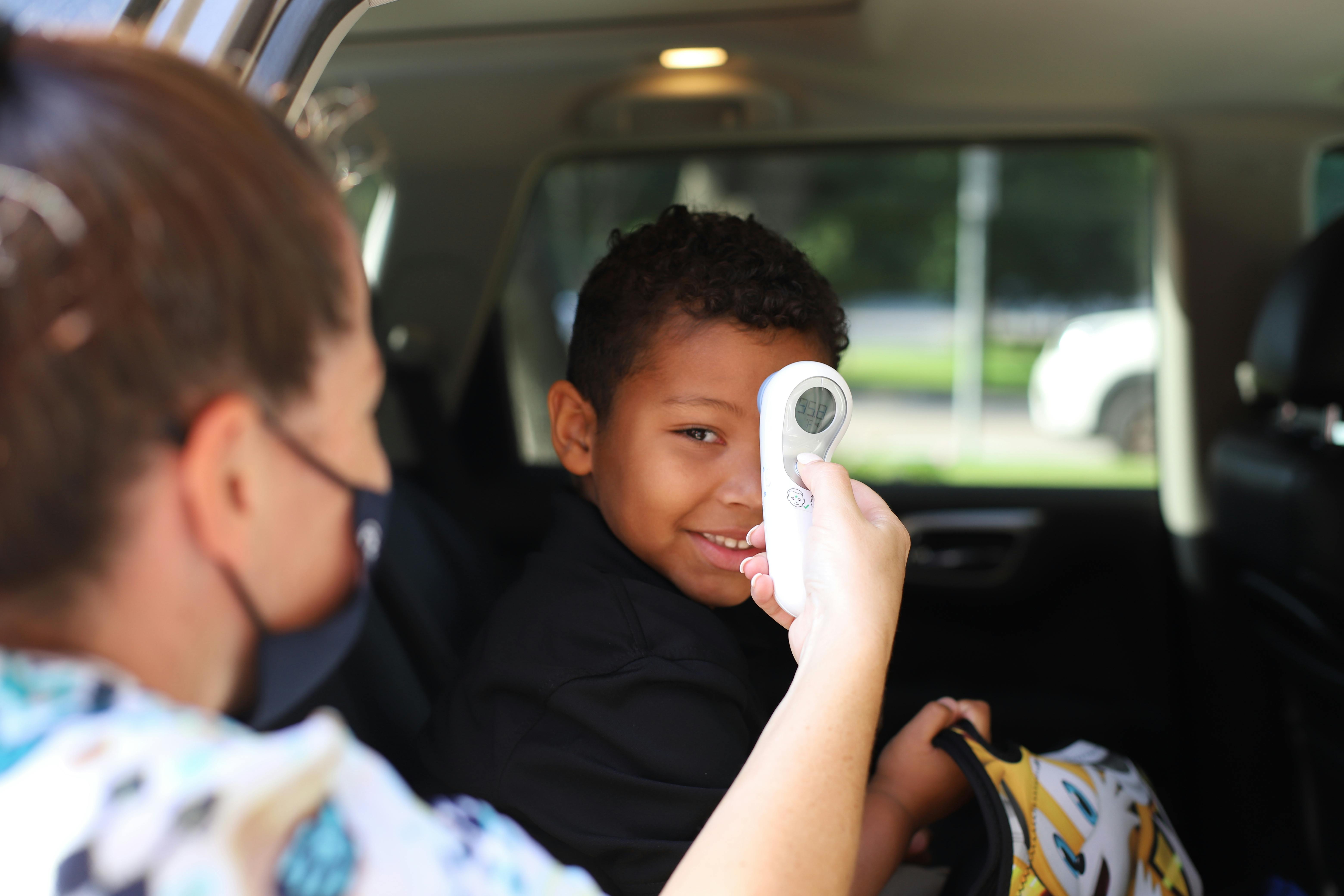 Person in mask taking a child's temperature with a thermometer in a car