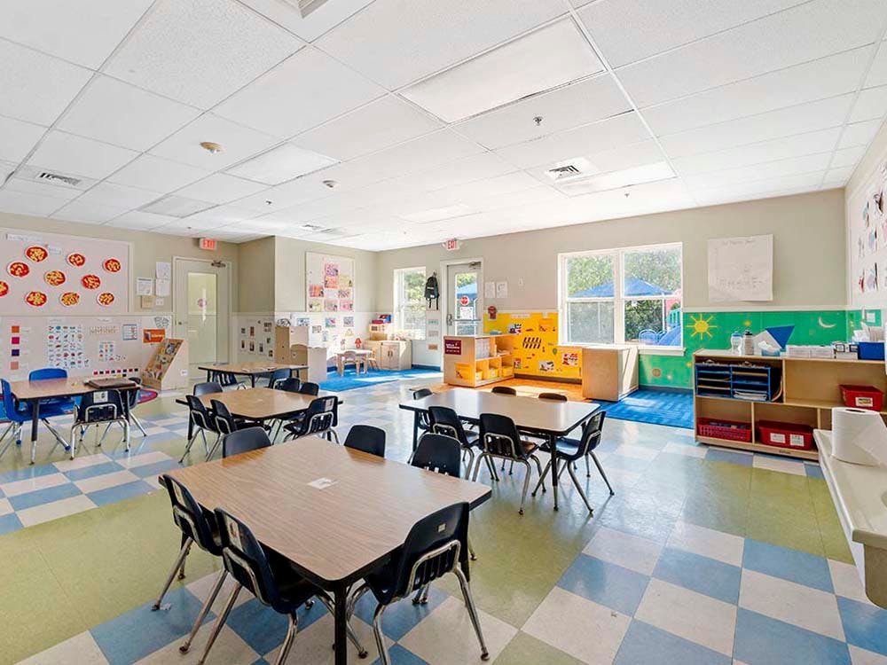 Empty classroom with small tables and chairs, toys, and art on walls