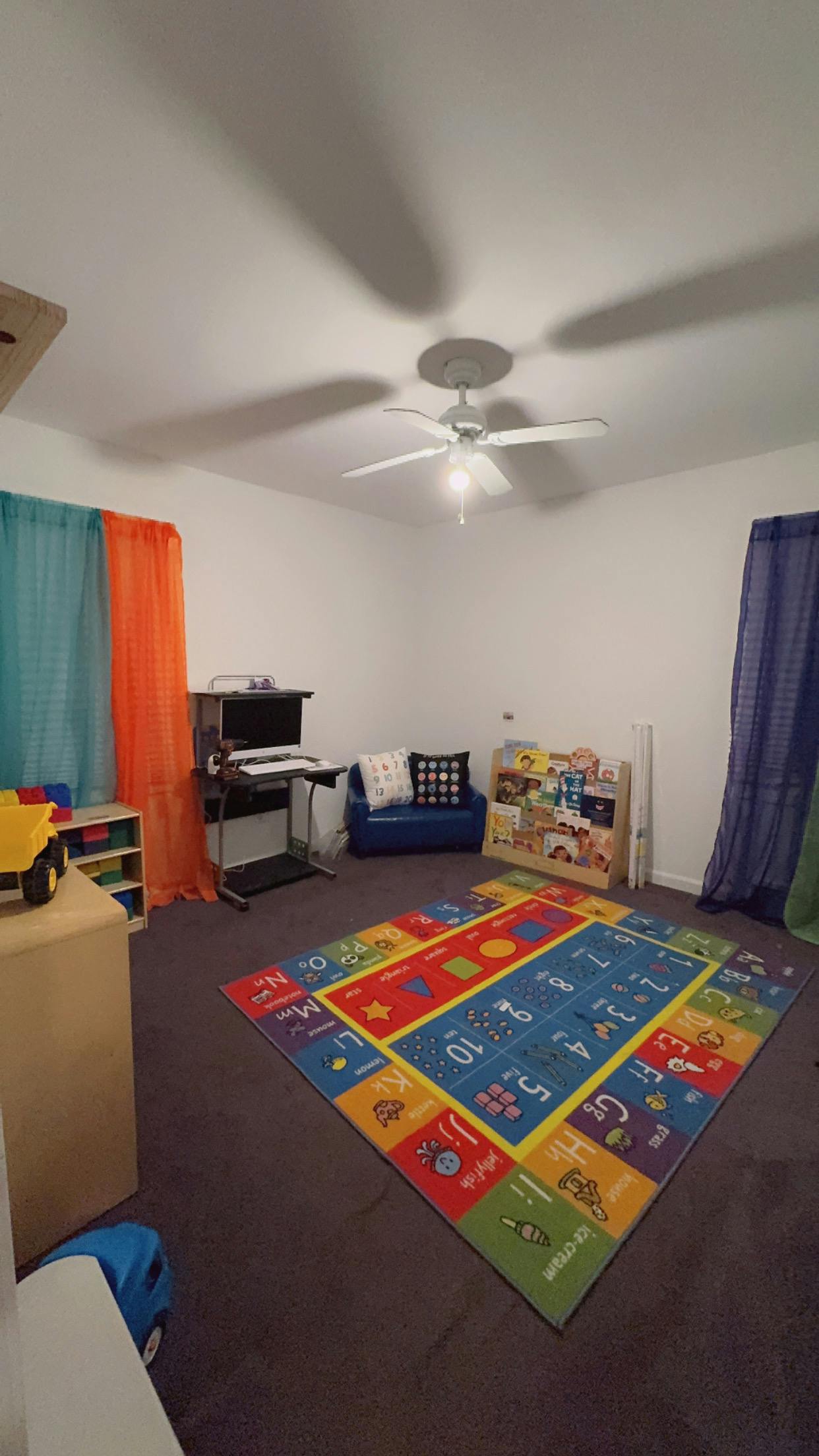 Room with a colorful alphabet and number rug, computer desk, and small blue couch