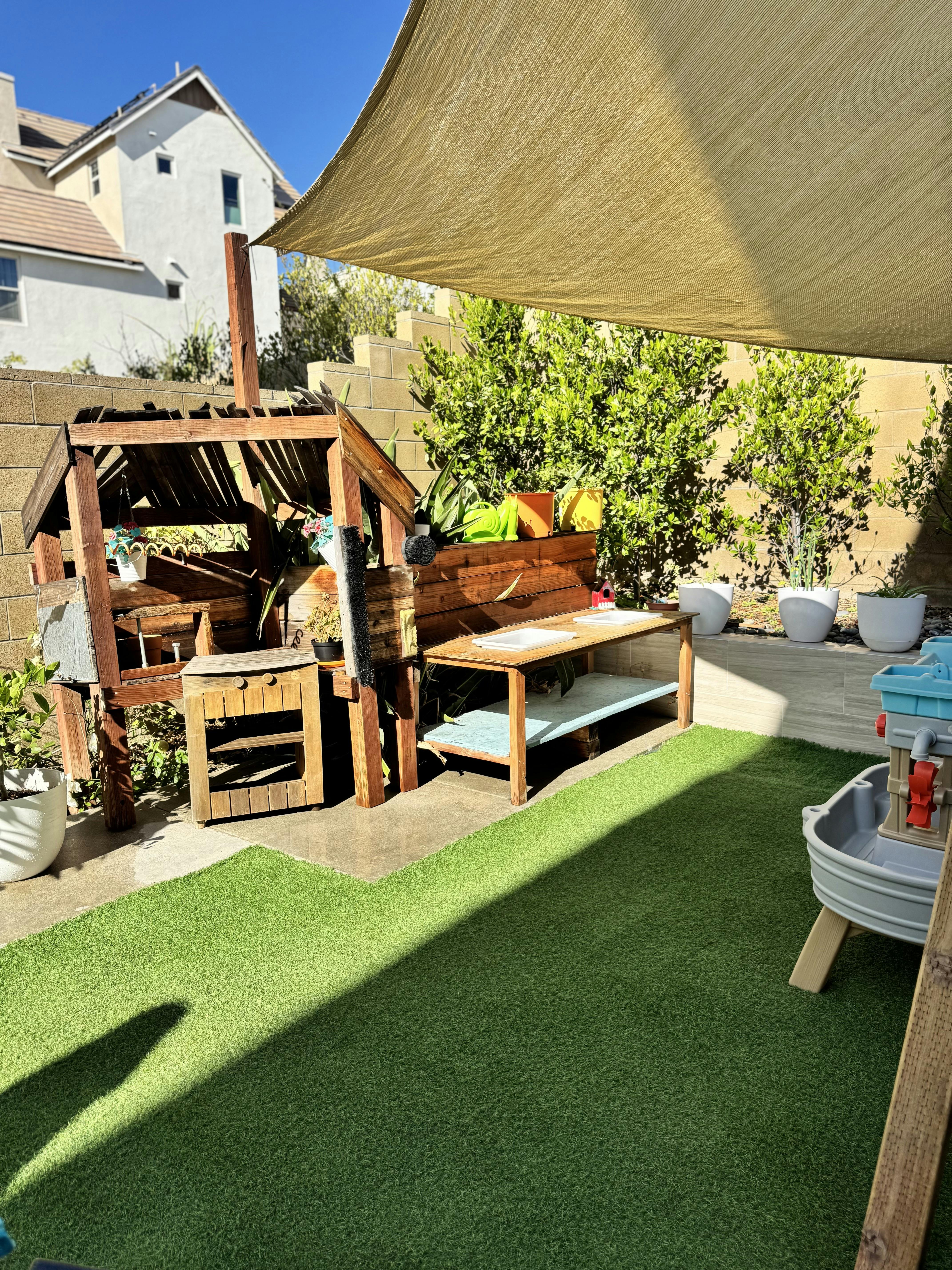 Wooden outdoor play structure with table and sandbox on a grass lawn