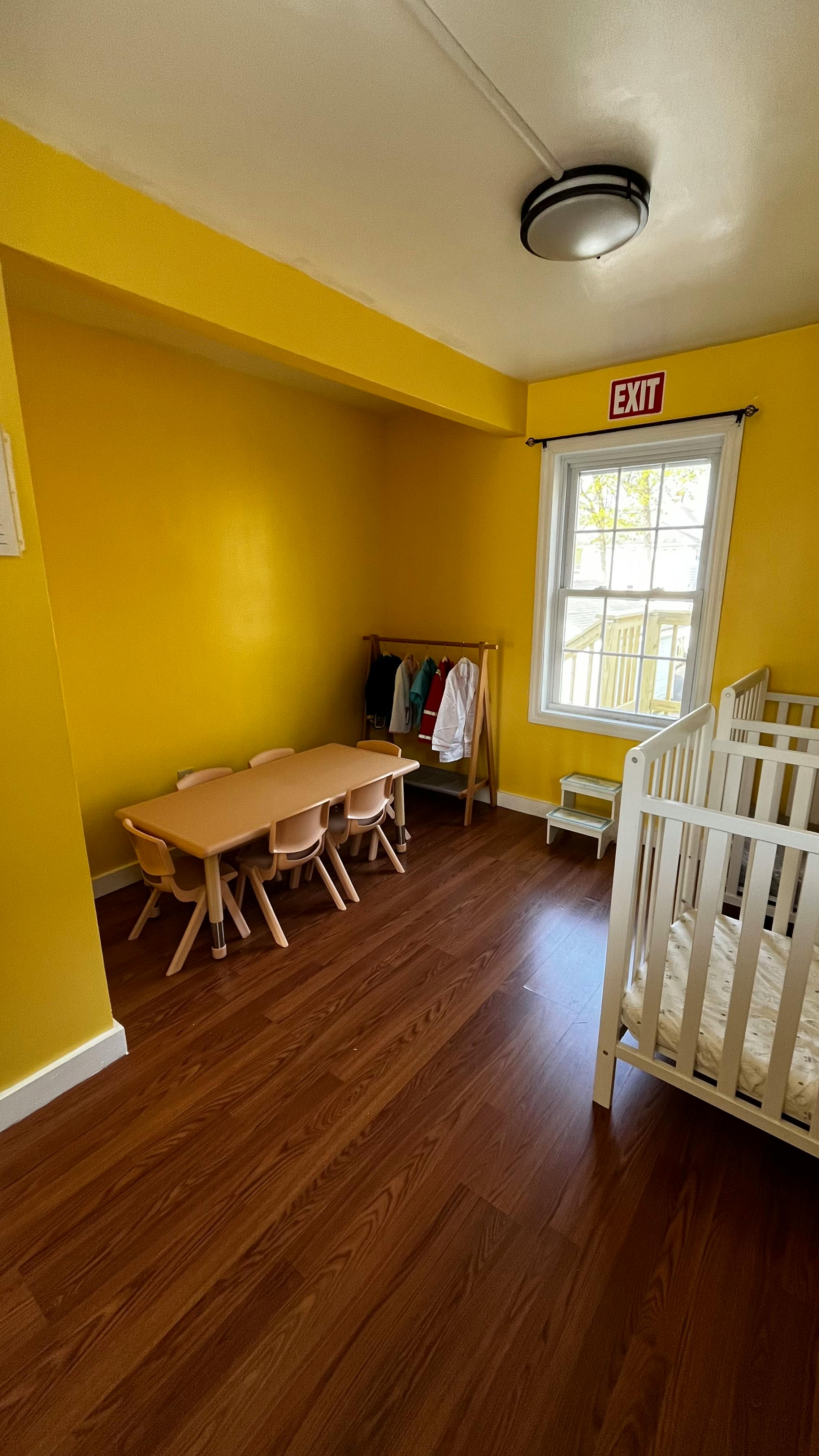 Classroom with small table and chairs, clothing rack, and two cribs