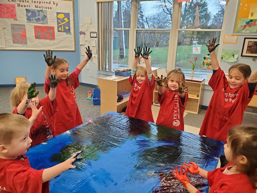 Children in red shirts with paint on their hands in a classroom
