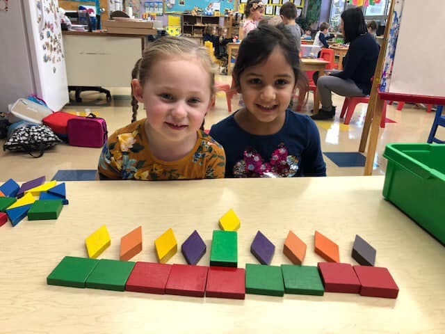 Two children at a table with colorful geometric blocks arranged shapes