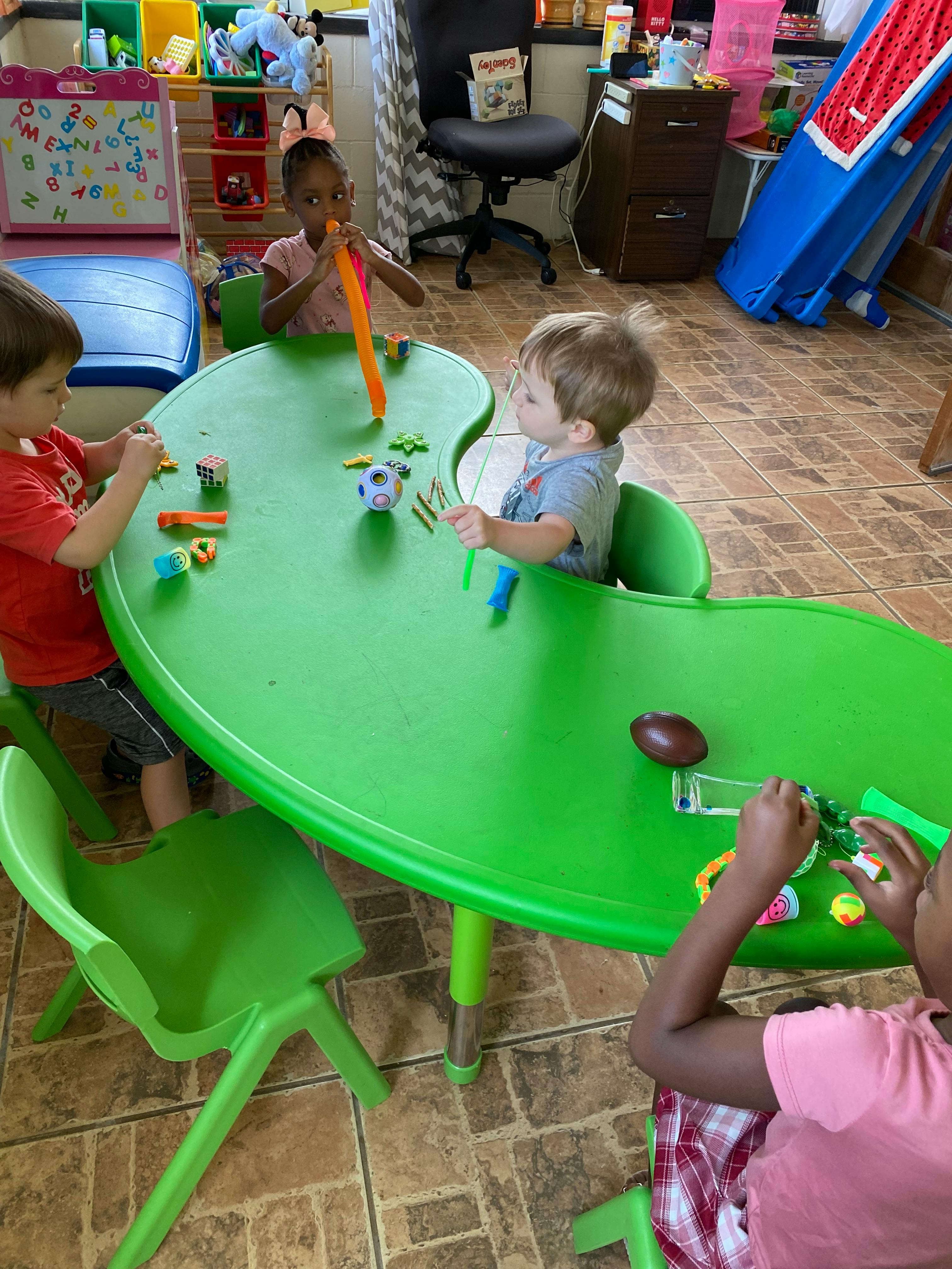 Four children sitting at a green table playing with various small toys