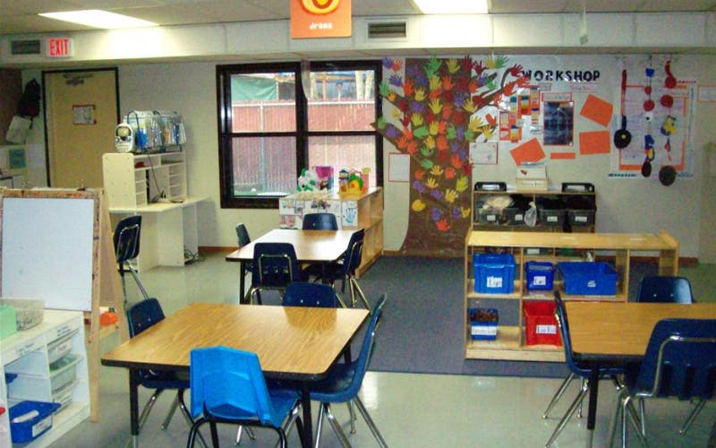 Empty classroom with small tables and chairs, and a handprint tree