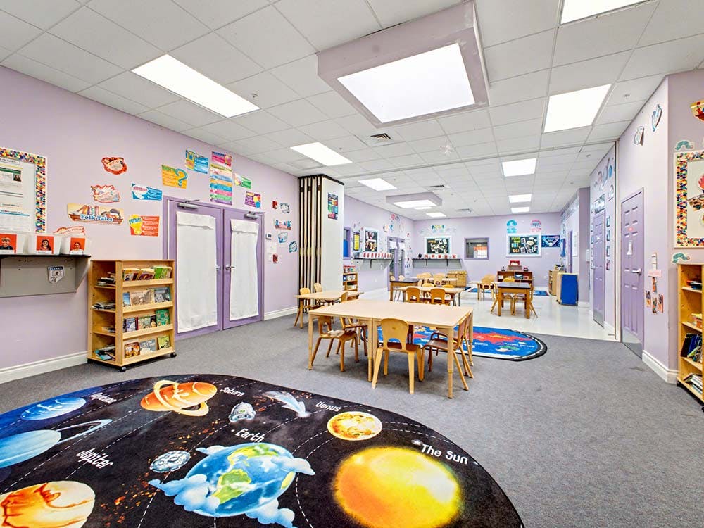 Empty colorful preschool classroom with small tables and chairs, solar system rug