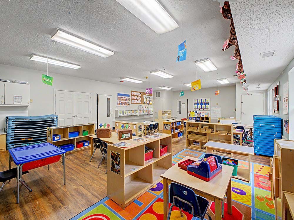Classroom with small tables, chairs, shelving units, and a colorful rug