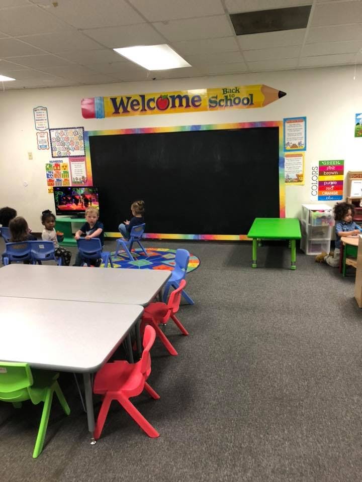 Children sitting in a classroom with a large blackboard and a "Welcome Back to School" sign