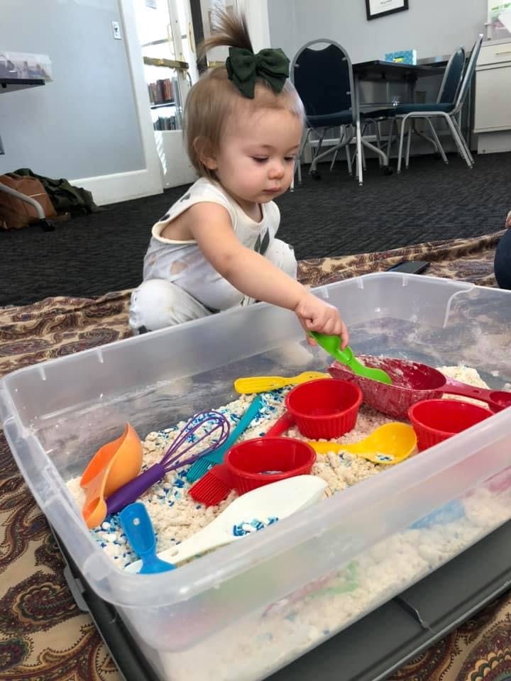 Child playing with sensory bin with colorful scoops and cups