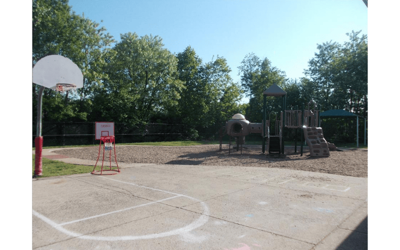 Basketball court with a playground and trees in the background