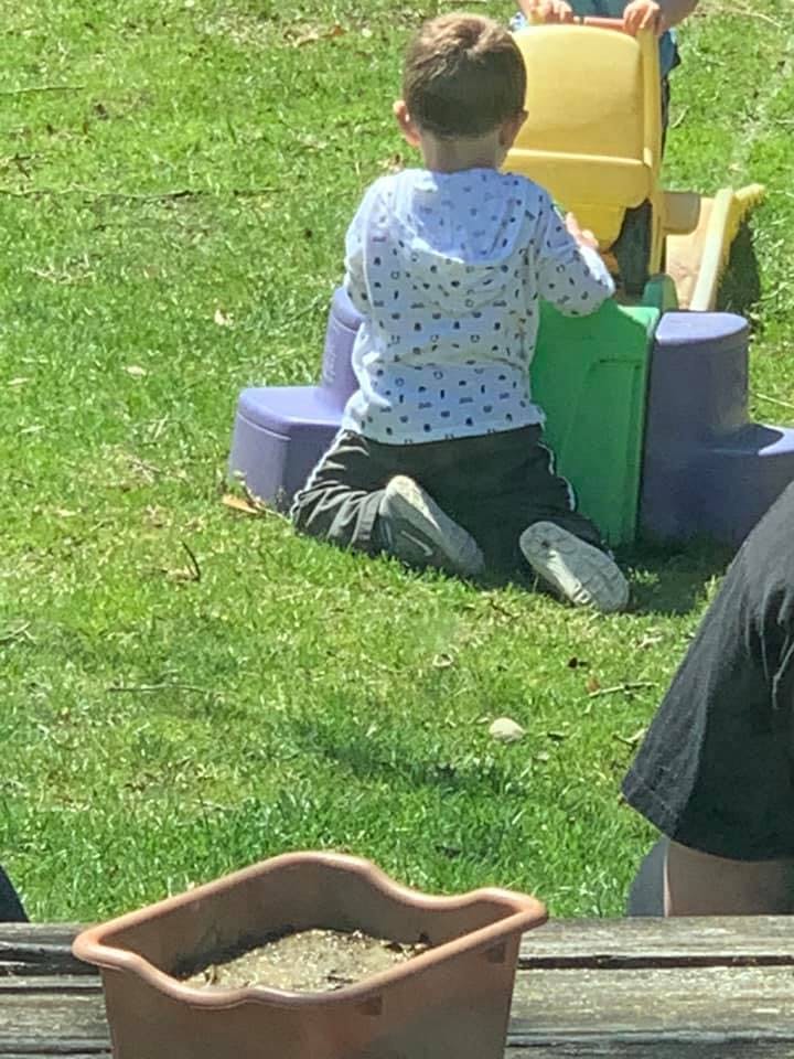 Child kneeling on grass playing with colorful plastic toys