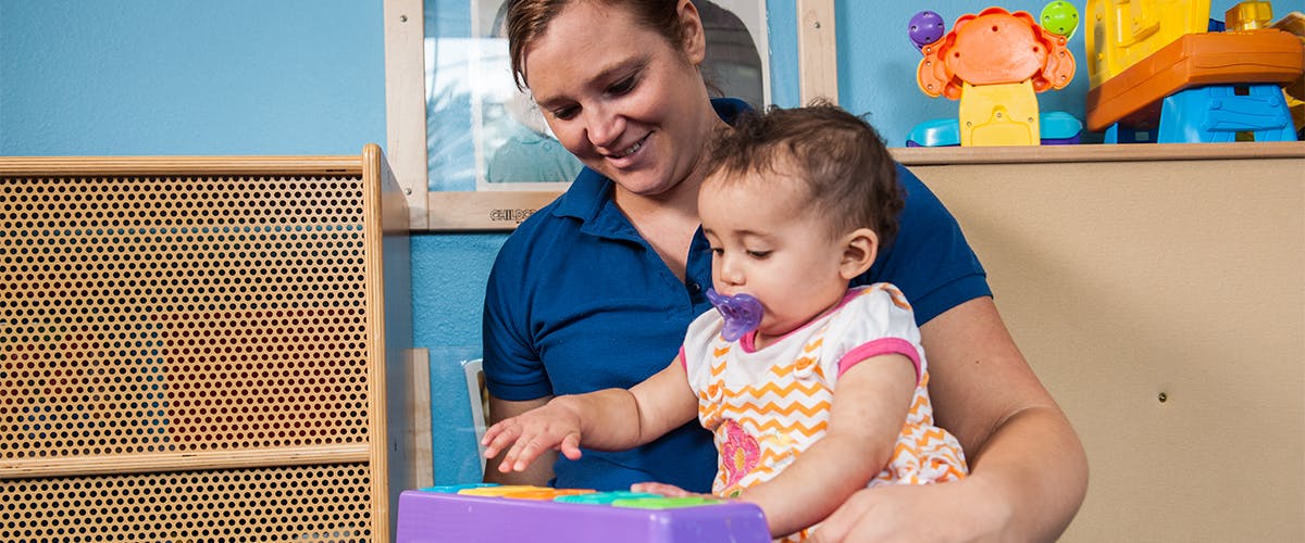 Person holding a child with a pacifier playing with a toy