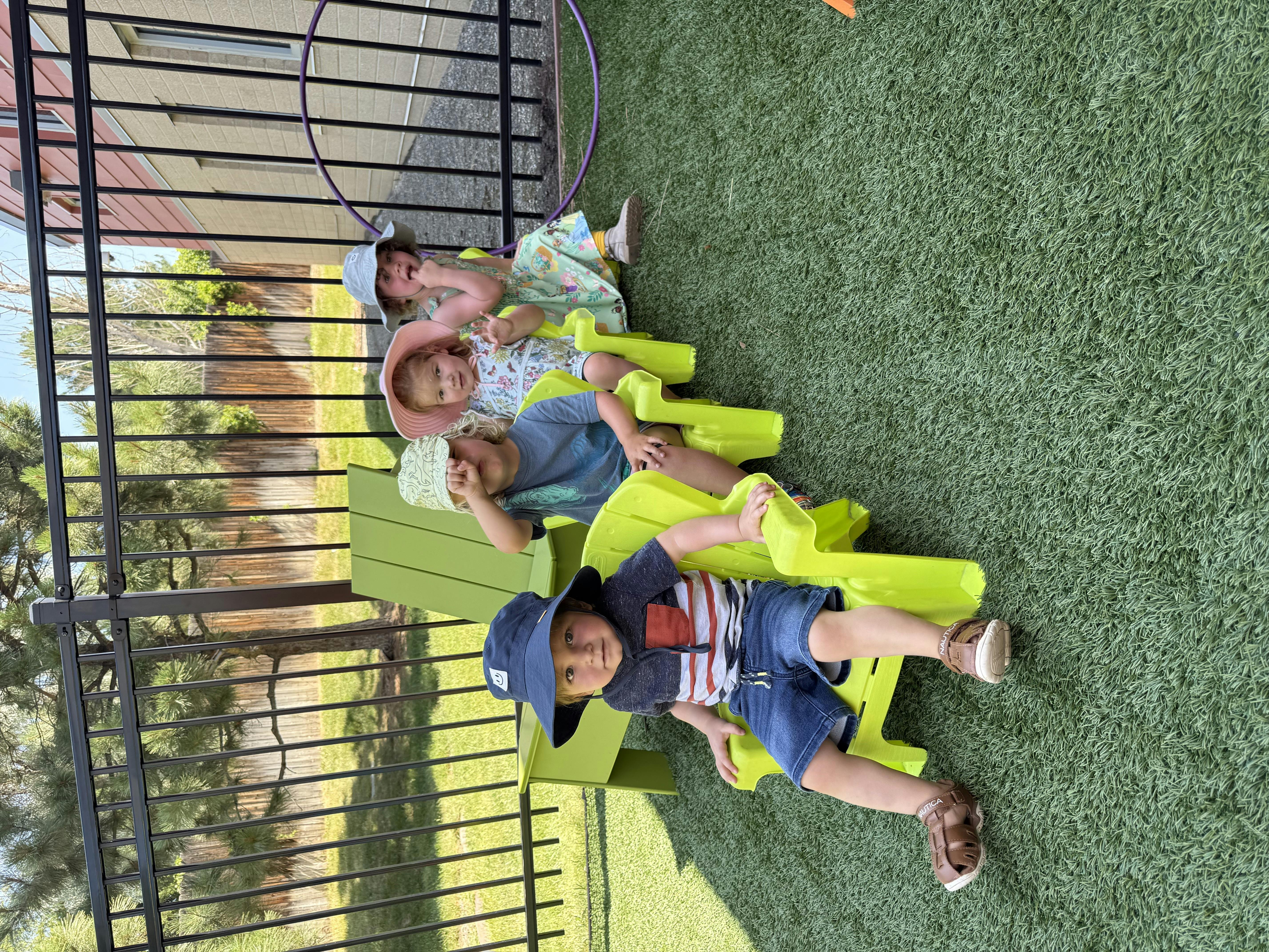 Four children sitting on green chairs outdoors