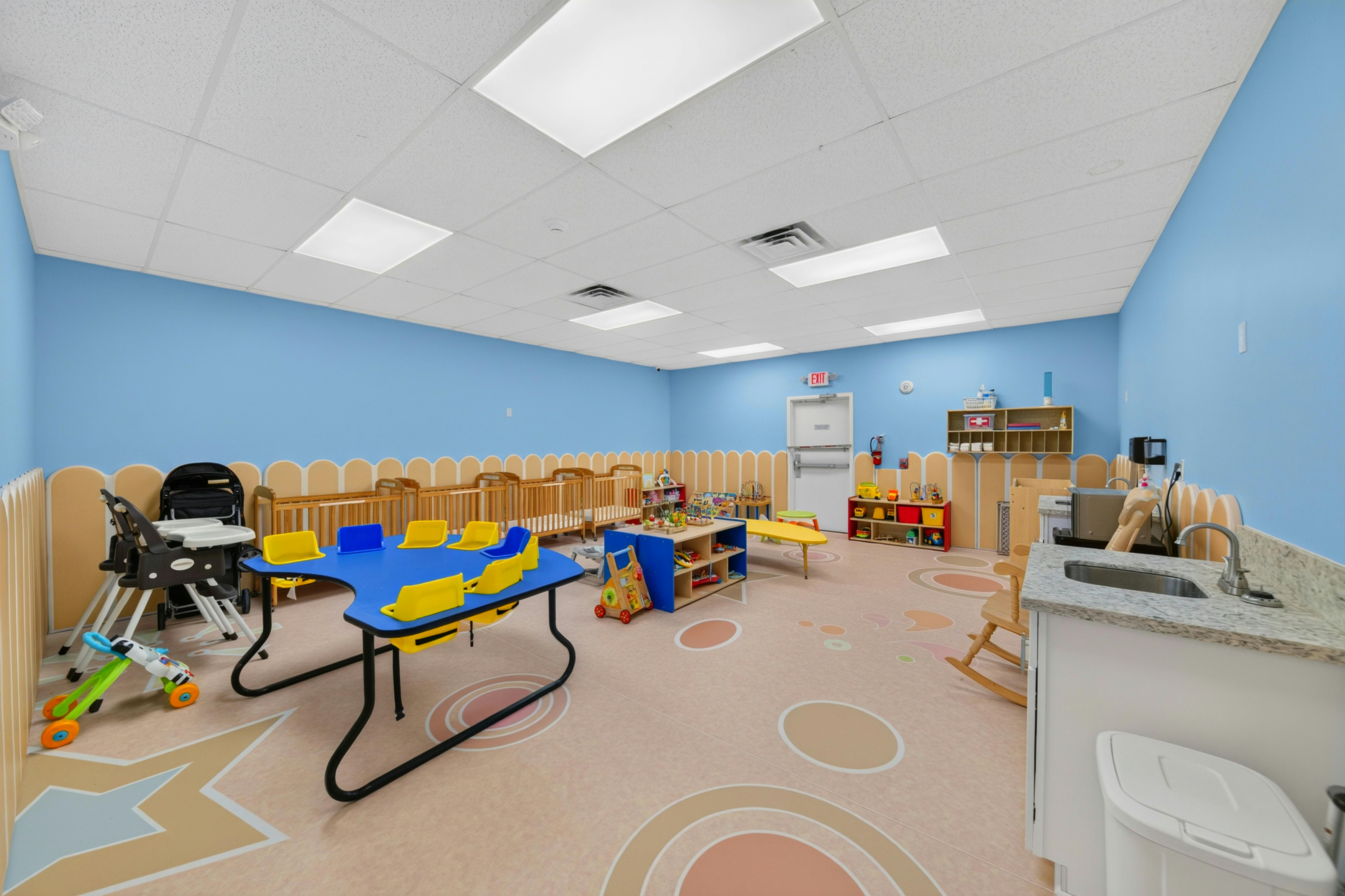 Childcare room with small tables, chairs, cribs, and play equipment