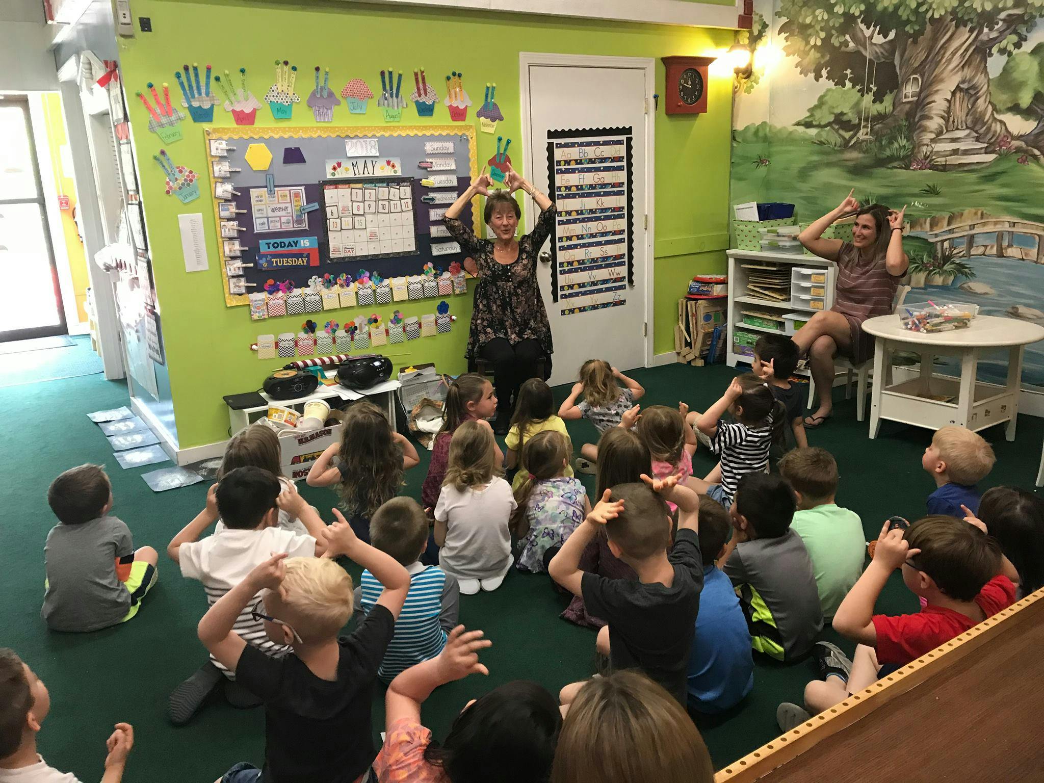 Two people leading a group of children in an activity in a classroom