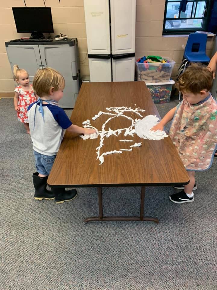 Two children playing with shaving cream on a table