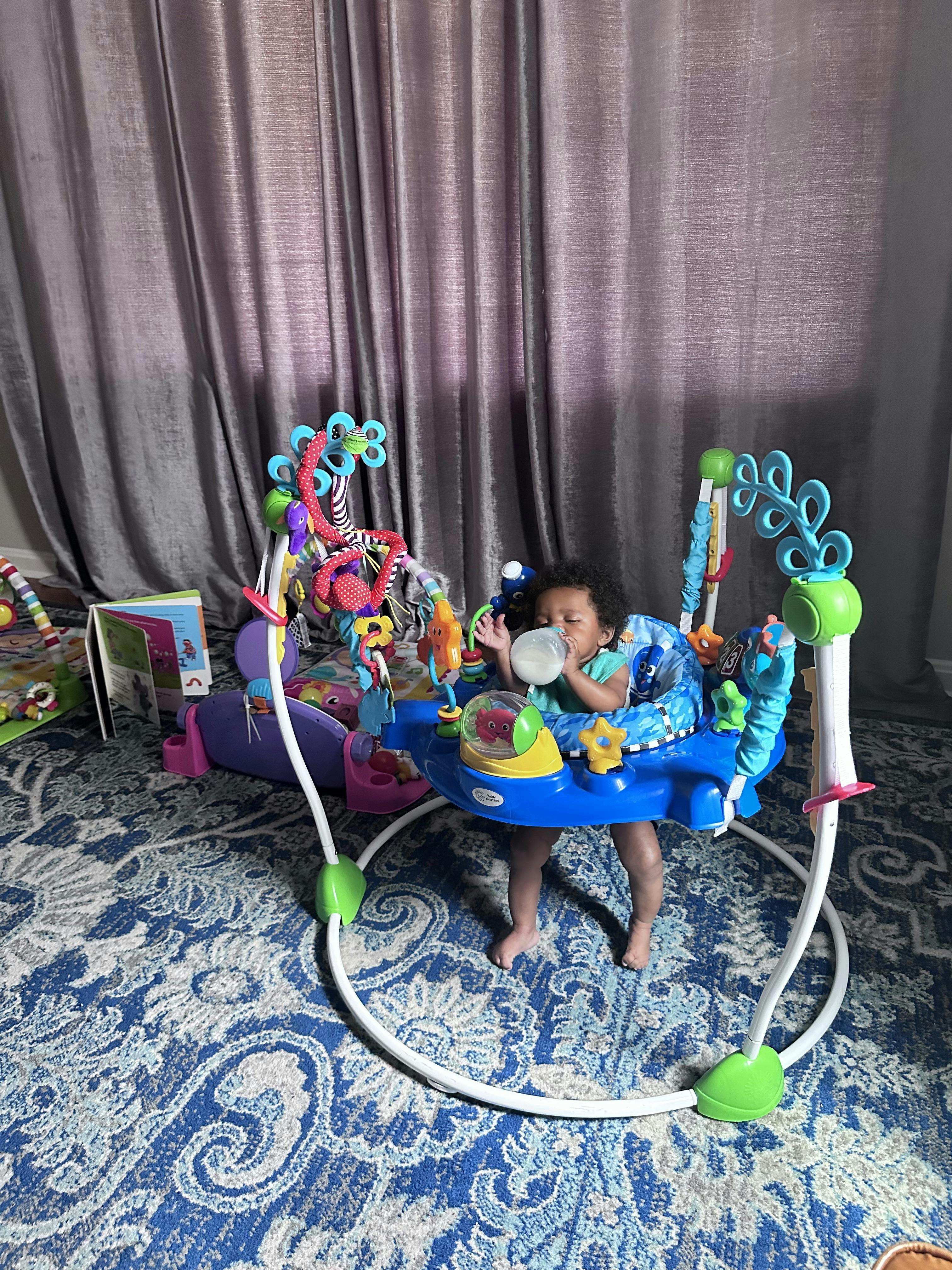 Child in a blue baby bouncer drinking from a bottle