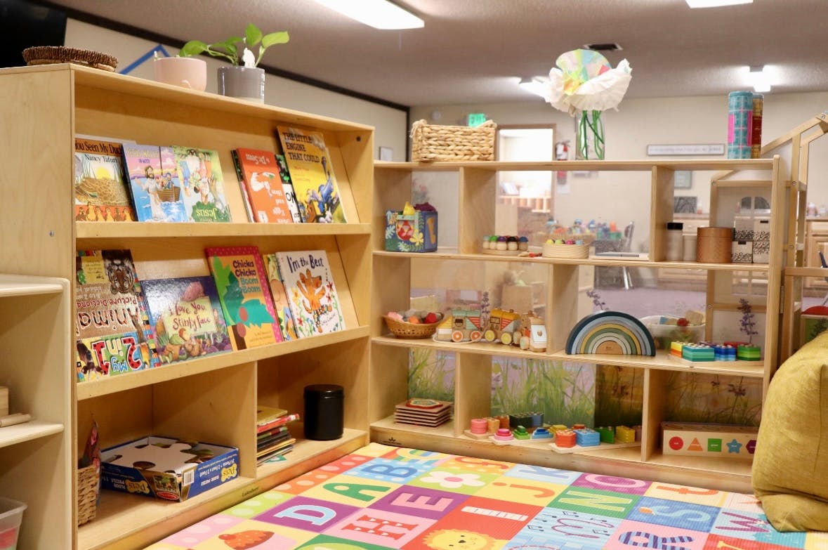 Children's books and toys on shelves with an alphabet playmat on the floor