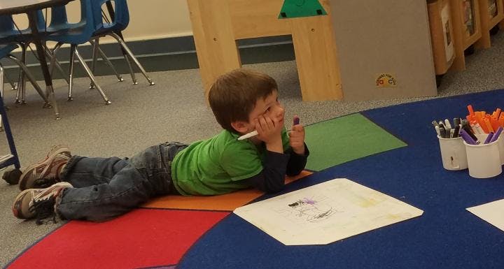 Child lying on floor drawing on paper