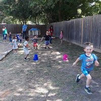 Child running on dirt with other children and adults in background