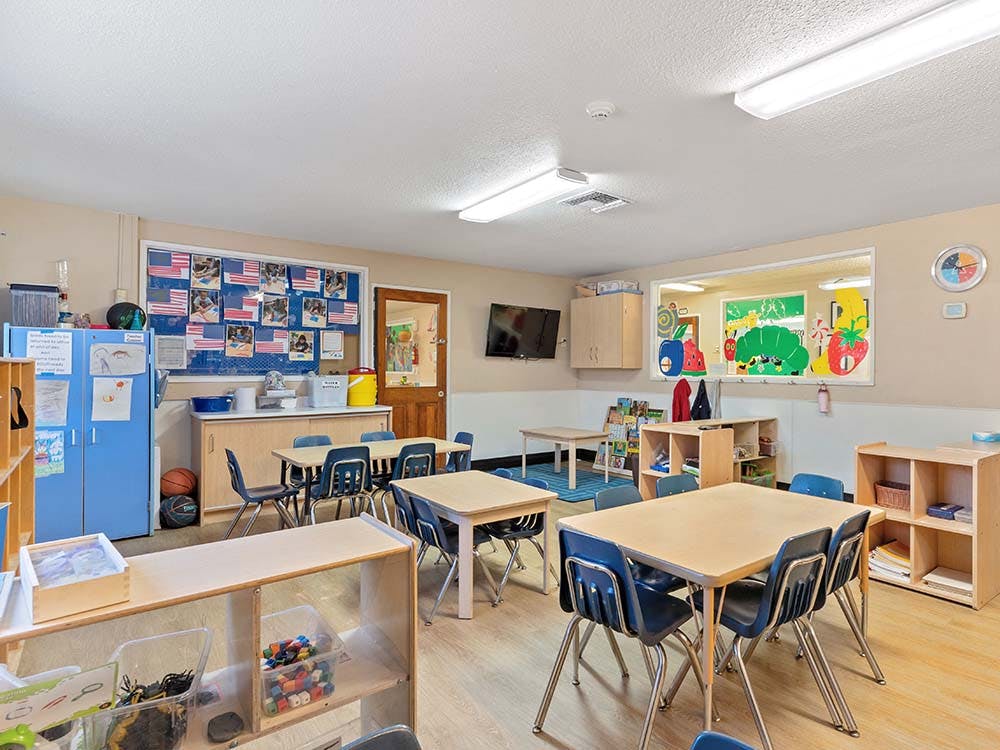 An empty classroom with several small tables and chairs
