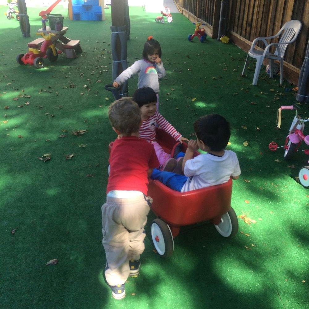 Children playing with a red wagon on green turf