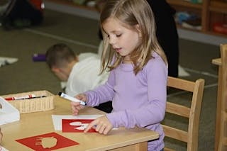 Child drawing on red paper at a desk