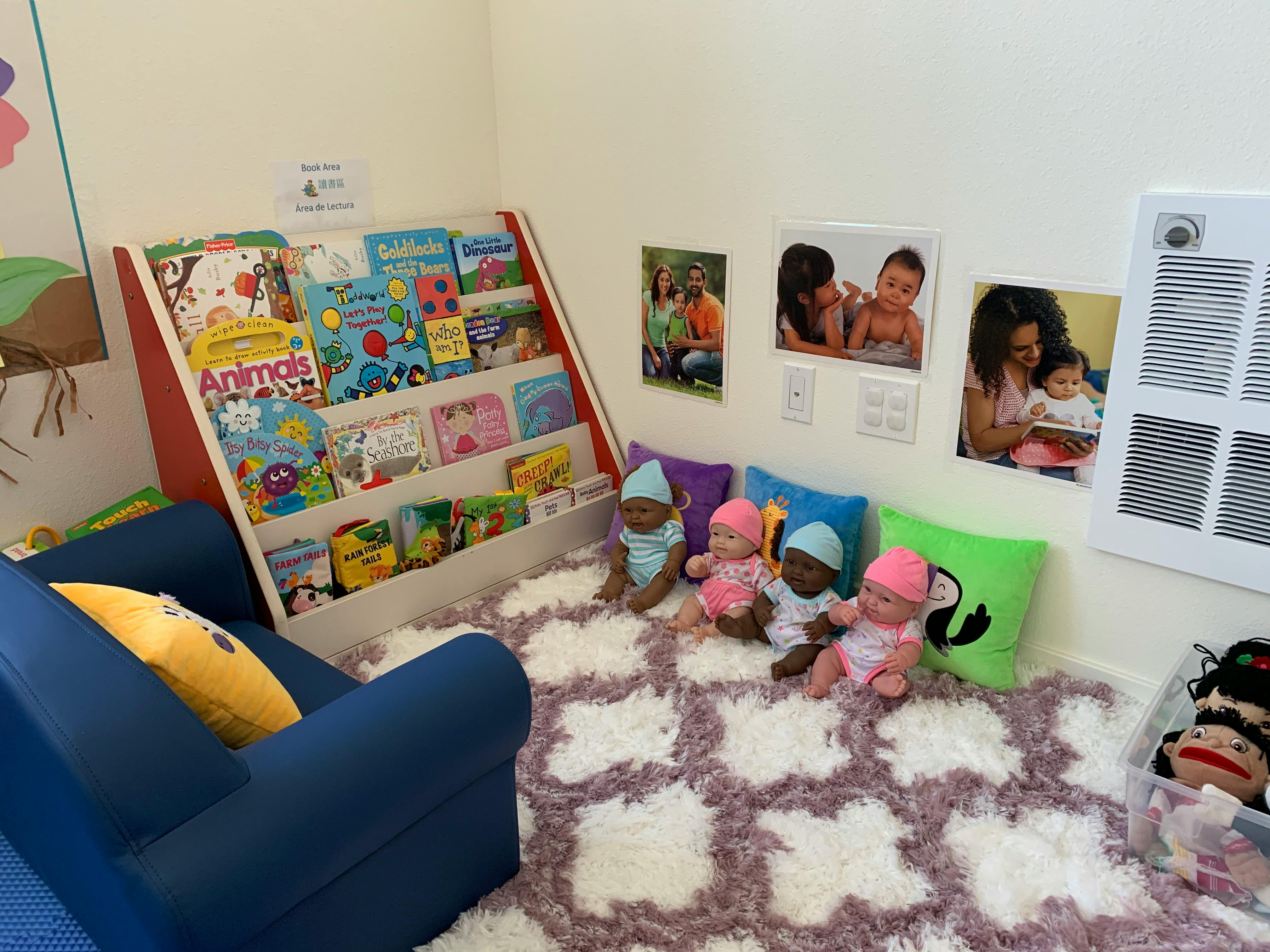Children's reading nook with a bookshelf, blue chair, and dolls on a rug