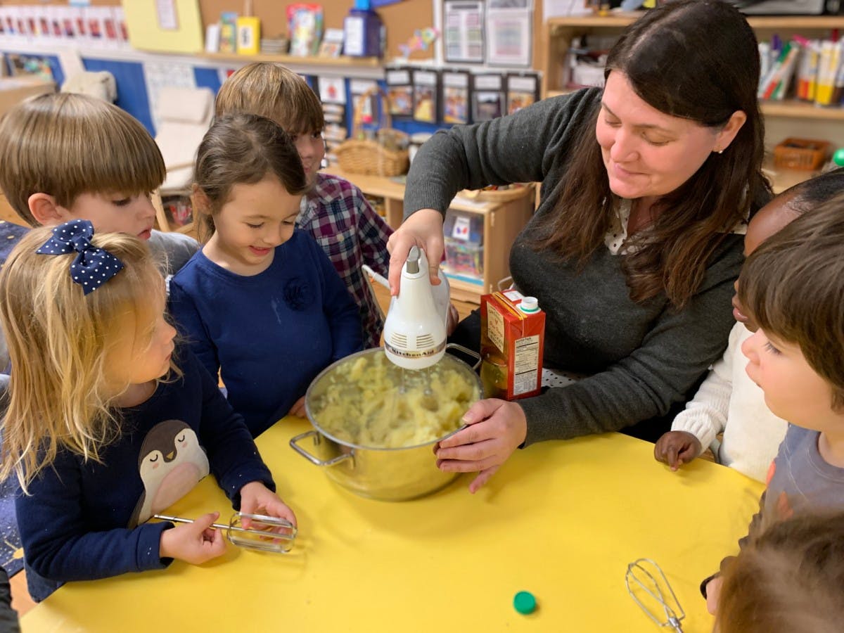 Adult using a hand mixer in a bowl with children watching