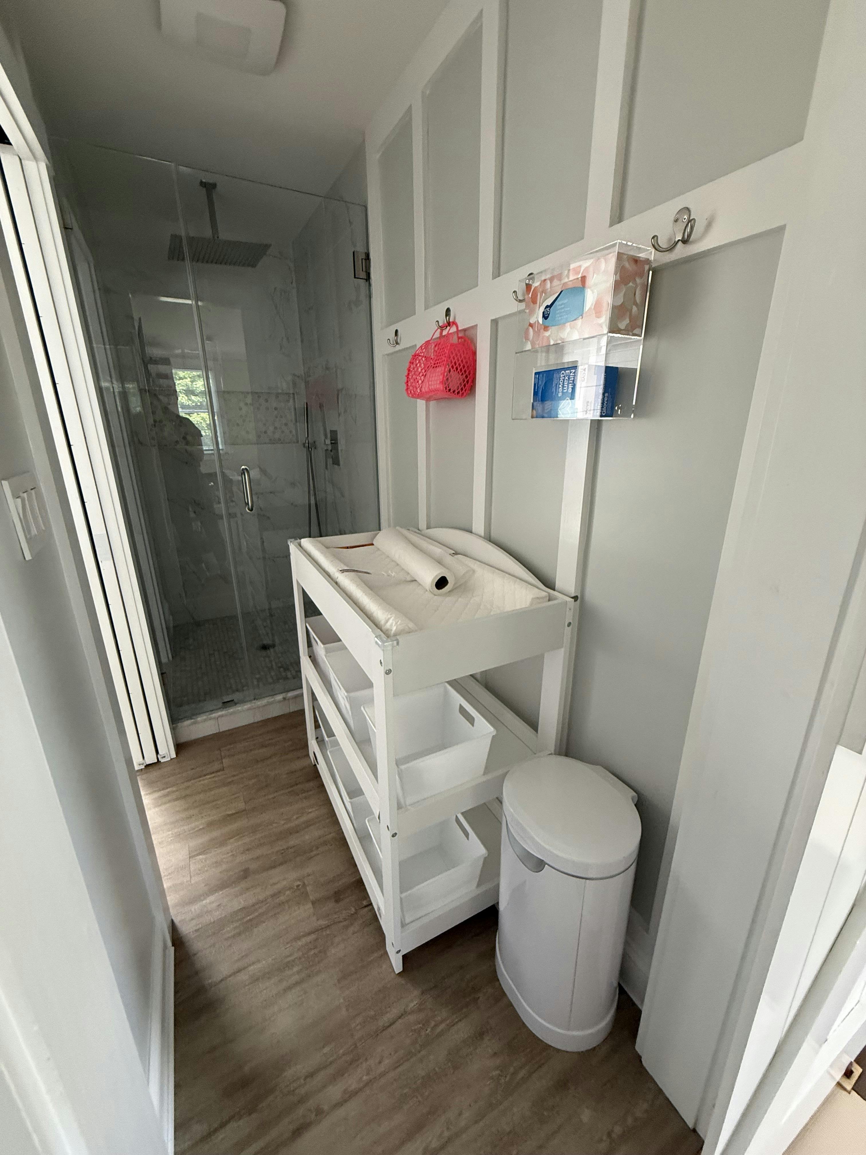 White changing table with baskets and waste bin in a bathroom