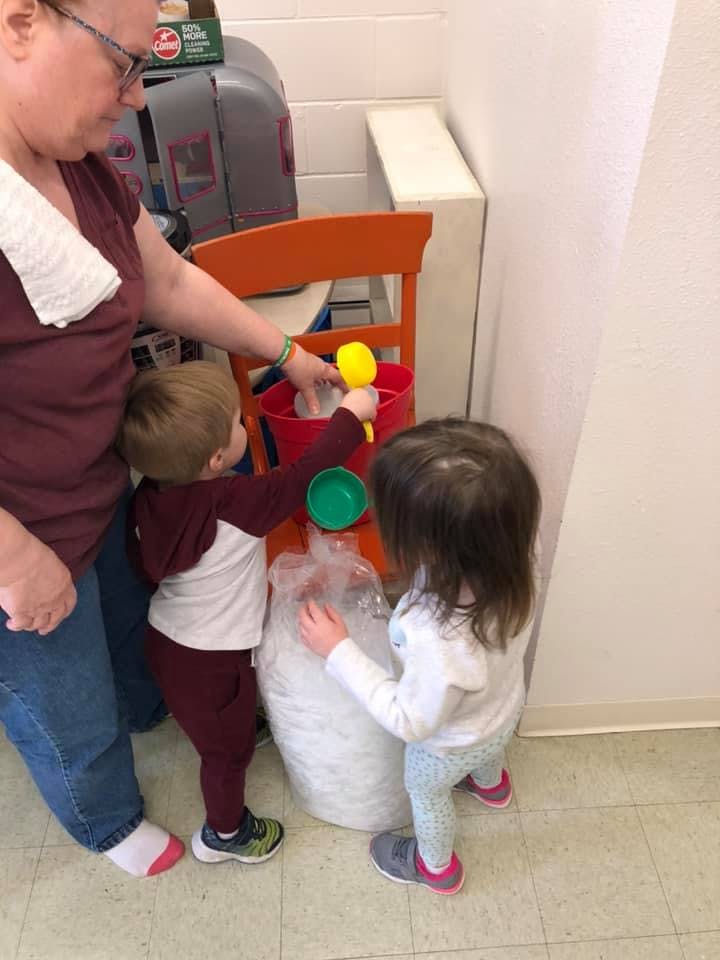 Adult and two children playing with a bucket and a bag of white material