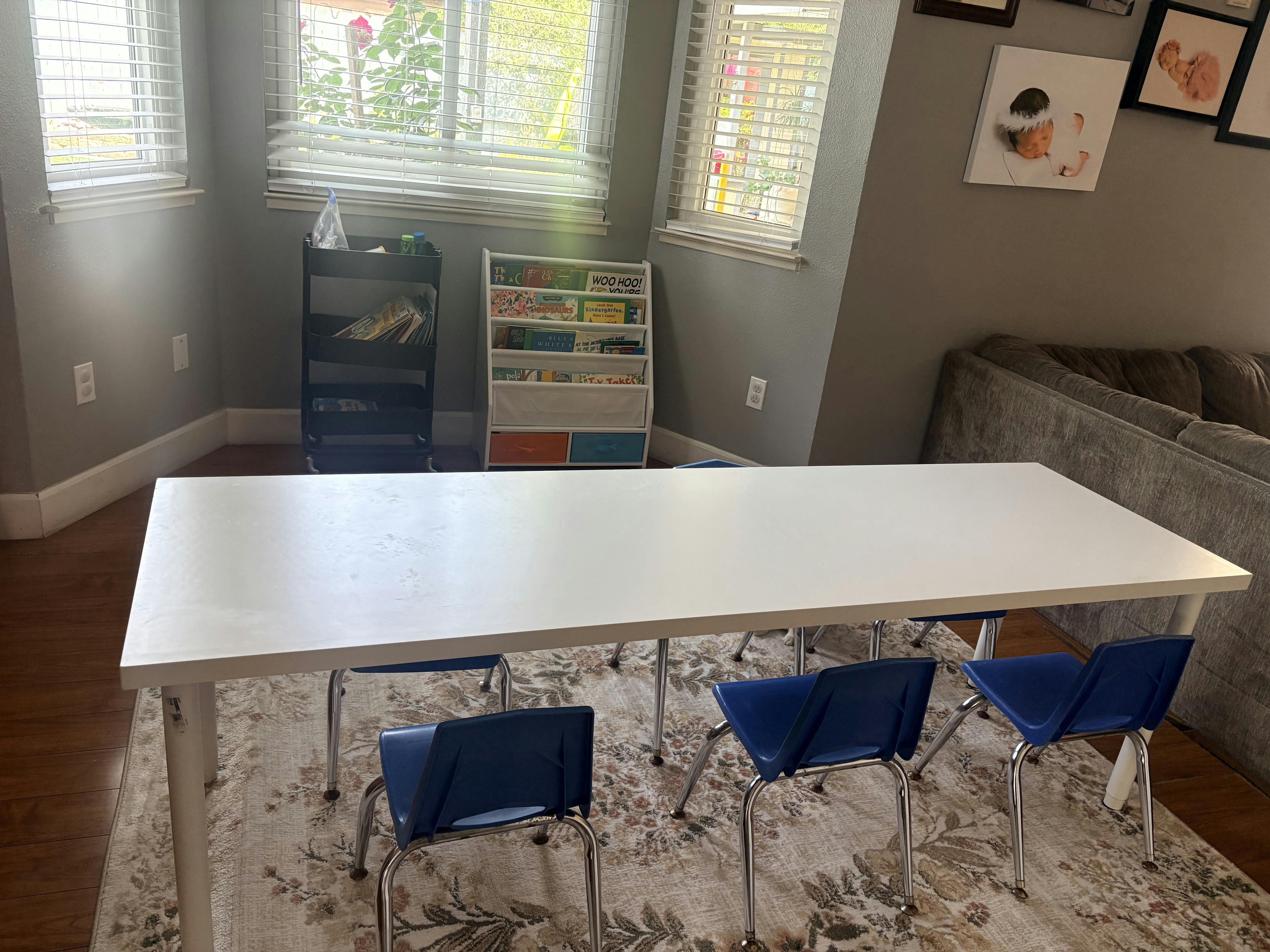 A long white table with several blue child sized chairs on a patterned rug