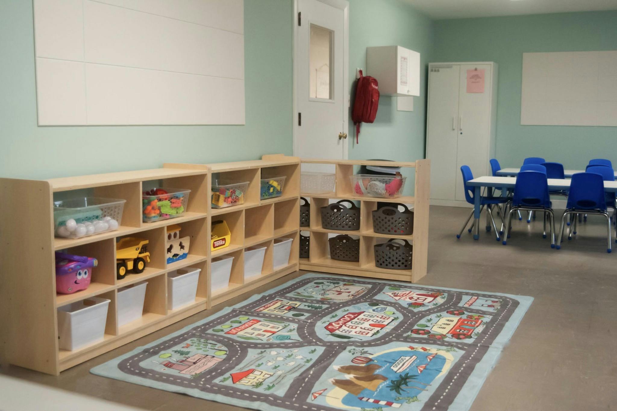 Classroom with toy shelves, play rug, and small tables with chairs