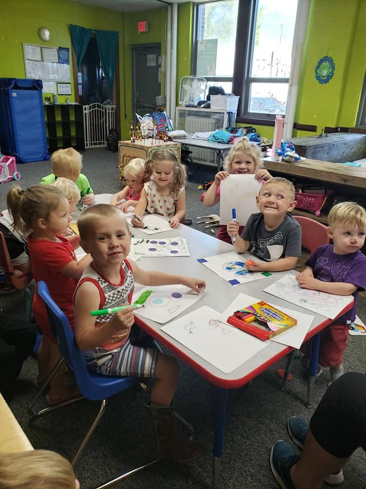 Children sitting at a table drawing and coloring in a classroom