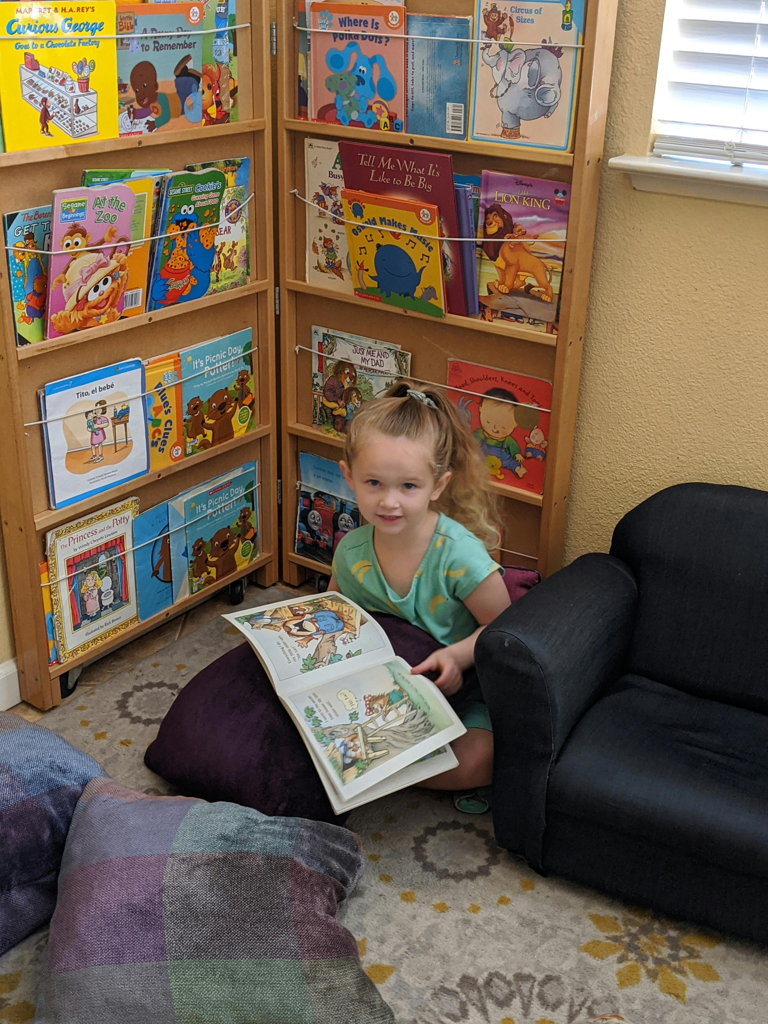 Child sitting on floor reading a book next to a bookshelf